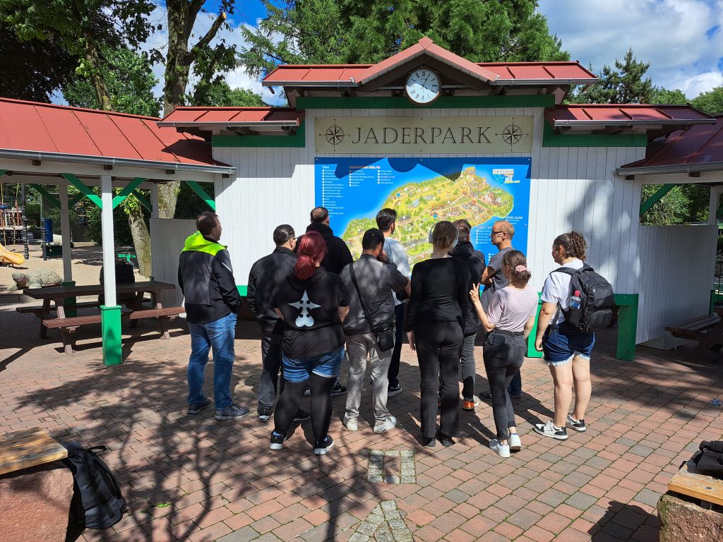 Ausflug von elf Teilnehmenden in den Jaderpark. Die Personen schauen sich den Lageplan an und sind mit dem Rücken zur Kamera gedreht.